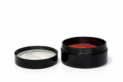 Two black cosmetic jars, one open with a white cream and the other with a red substance, on a white background.